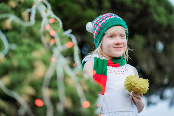 little blonde hispanic latina girl smiling and wearing christmas clothes outdoors holding a flower in her hand