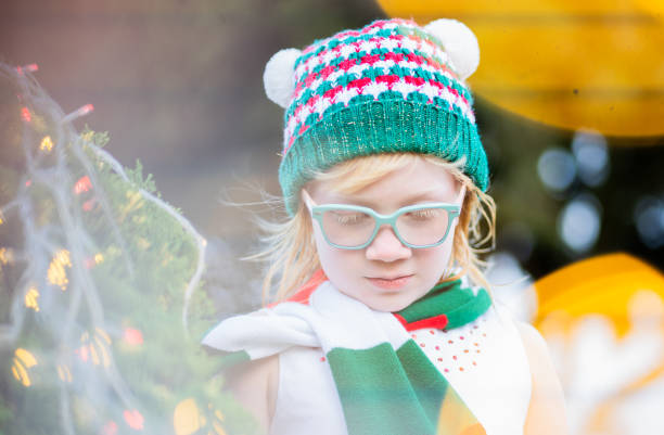 little blonde girl in christmas wearing coat and glasses while standing outdoors