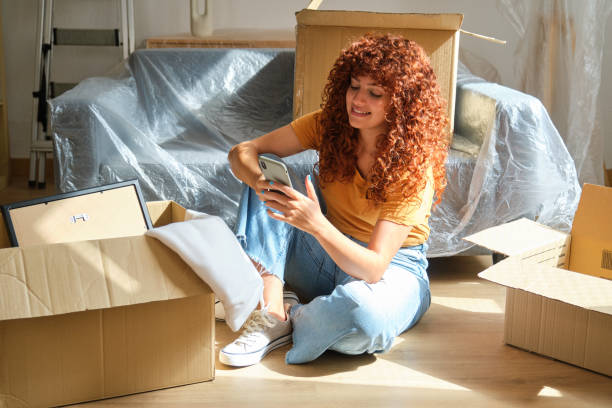 istock Young woman using smartphone while taking a break from moving into new home 2170387562