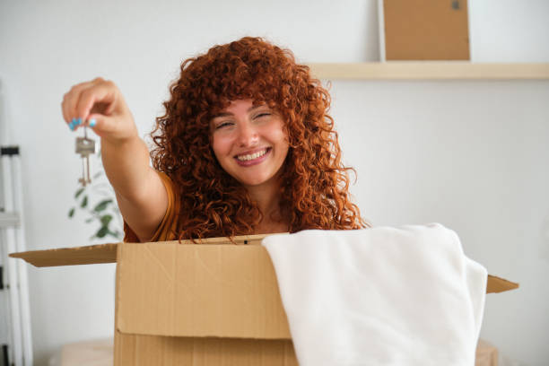istock Woman holding keys and smiling behind cardboard box 2170387720