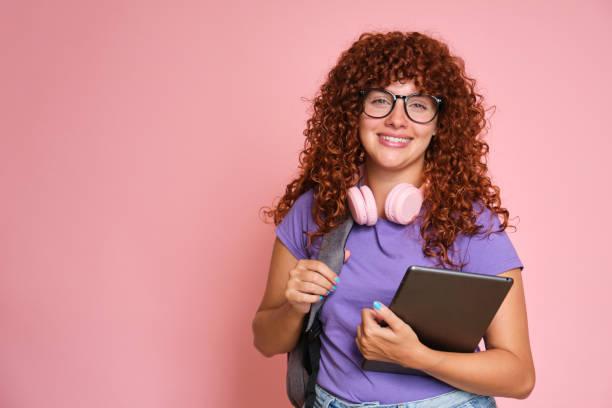 istock Happy student with curly red hair is holding a tablet and carrying a backpack 2170389333