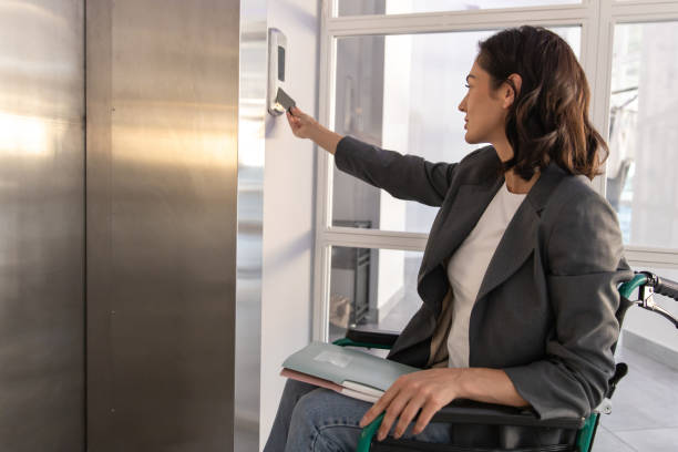 istock Woman sitting on wheelchair and pushing sensor button for call the elevator in office 2170390545