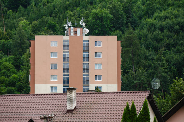 A modern apartment building with a flat facade, featuring minimal windows and a prominent central chimney. The building has a simple design with light beige walls and glass-enclosed balconies, set against a partly cloudy sky.
