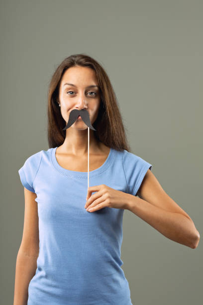 istock Young woman holding fake mustache on grey background 2170396742