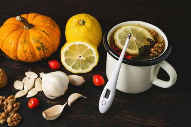 Cold and flu season and alternative medicine, natural remedies, digital thermometer, cup of herbal tea, lemon, garlic, pumpkin seeds, walnuts and dog rose fruit on a dark wooden background Cold and flu season and alternative medicine, natural remedies, digital thermometer, cup of herbal tea, lemon, garlic, pumpkin seeds, walnuts and dog rose fruit on a dark wooden background. food sample cups stock pictures, royalty-free photos & images