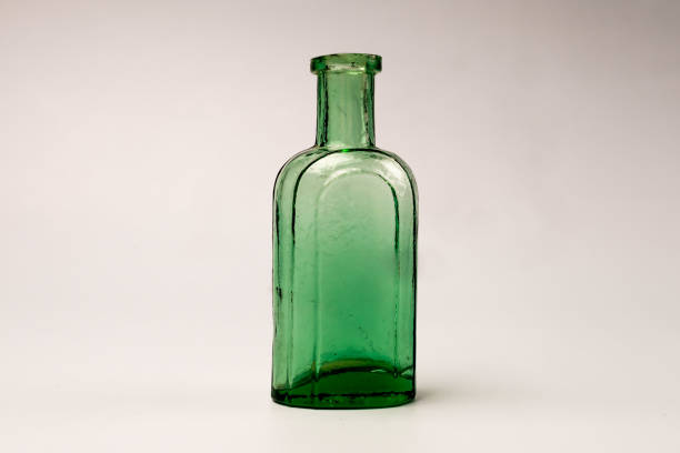 A green glass bottle sits on a bright windowsill, illuminated by sunlight. The view includes blurred, natural scenery beyond the window, adding depth and a timeless feel to the image.