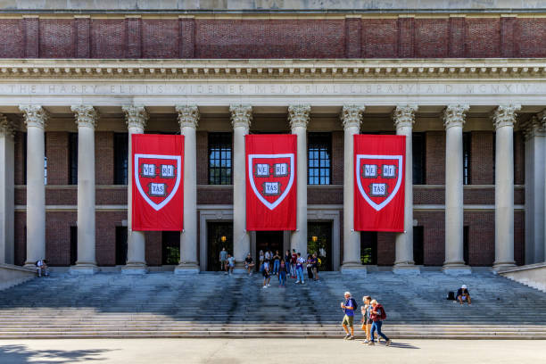 Cambridge, Massachusetts, USA - August 31, 2024: Crowd of people  in front of the Harry Elkins Widener Memorial Library (c. 1915). Harvard VERITAS shield banners hang in front of building. The library houses some 3.5 million books in its stacks and is the center­piece of the Harvard College Libraries.  It honors 1907 Harvard College graduate and book collector Harry Elkins Widener.