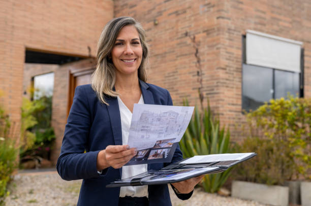 With a tranquil garden backdrop, a woman aims her tablet at the exterior of a charming home, emphasizing the role of technology in modern home exploration and decision-making.