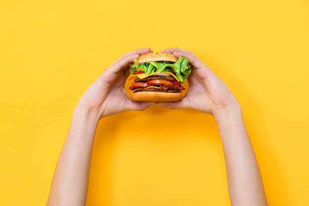 istock Two hands holding hamburger on yellow isolated background 2170461647