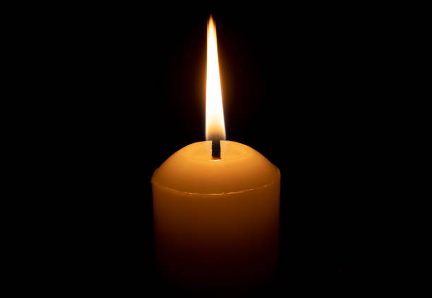 istock A single burning candle flame or light glowing on a big white candle isolated on red or dark background on table in church for Christmas, funeral or memorial service 2170465228
