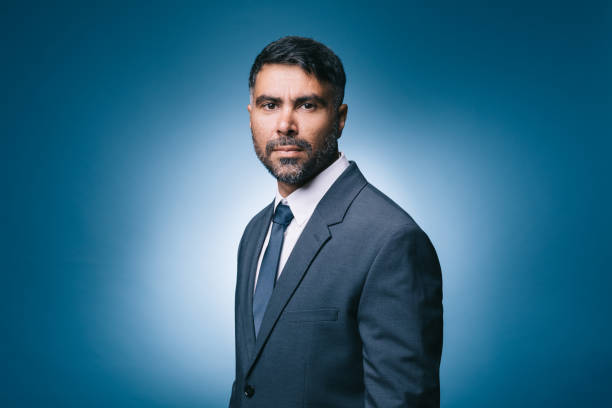 A mid-adult Indian businessman looks directly at the camera, his expression calm and confident, wearing a suit.