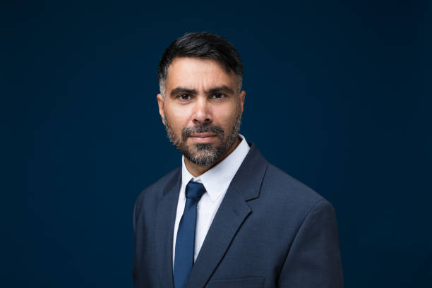 A mid-adult Indian businessman looks directly at the camera, his expression calm and confident, wearing a suit.