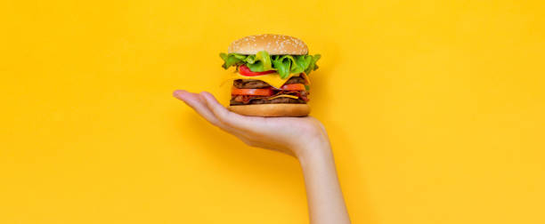 istock Hand holding cheeseburger on yellow isolated background 2170465610