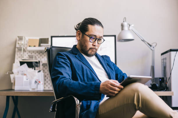 Asian creative looks at a digital tablet while sitting at his desk