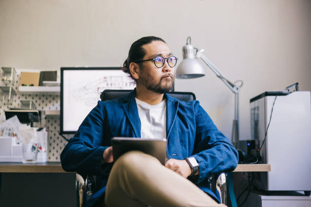 istock Asian creative sits at his desk, looking thoughtfully away from the camera 2170471949