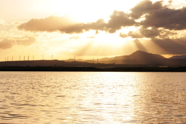The bright sun is shining beautifully through the scattered clouds above the calm water, creating a picturesque scene of natures beauty