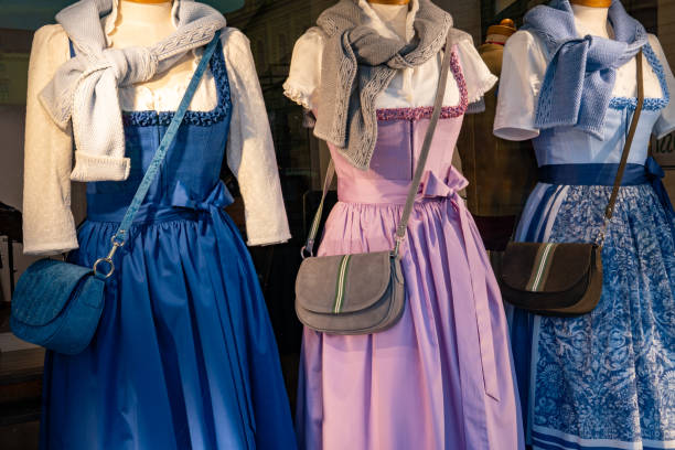 Three mannequins wearing dirndls (a Bavarian and Austrian traditional dress). Here, country-style dresses in blue and pink with a white blouse, apron and shoulder bag