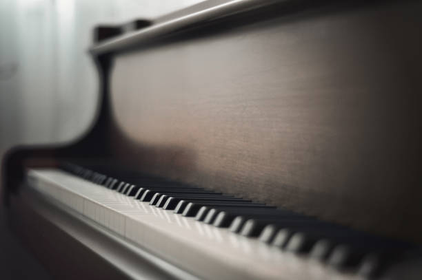 Close-up view of ivory colored keys of piano with opened lid, window with white curtains in the background.
