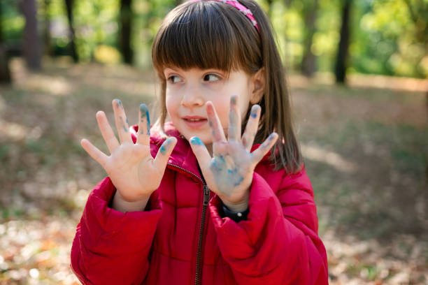 Cute little girl whit painted hands standing in public park in early autumn day