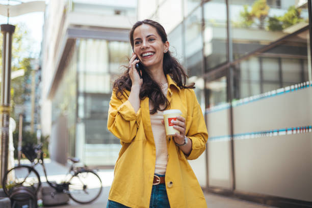 istock Happy Woman Talking on Smartphone While Holding Coffee Cup Outdoors 2170478416