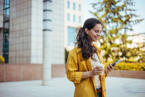 istock Smiling Woman in Yellow Jacket Using Smartphone Outdoors 2170478423