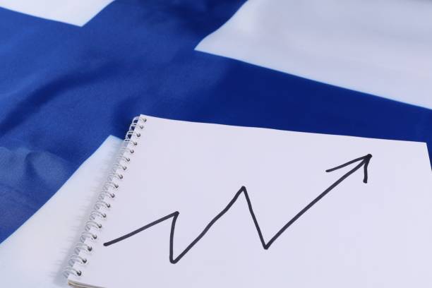 A notepad with a growth trend chart is placed next to the Finnish flag, illustrating economic progress or business development in Finland. The setting highlights national identity and prosperity.