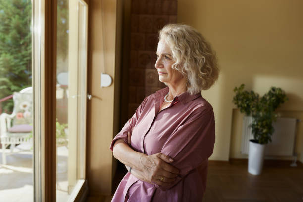 istock Pensive senior woman looking through window at home. 2170483969