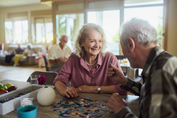 istock Happy mature couple talking while making jigsaw puzzle at nursing home. 2170484262