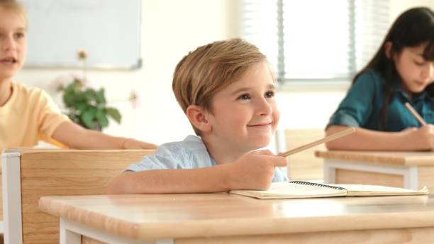 Smart caucasian boy raising hand for asking teacher at classroom. Pedagogy.