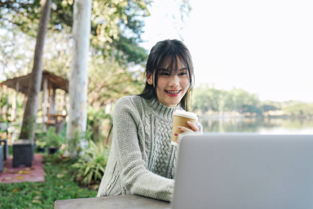 istock Young Woman Enjoying Coffee While Working on Laptop Outdoors in a Serene Park Setting 2170491730
