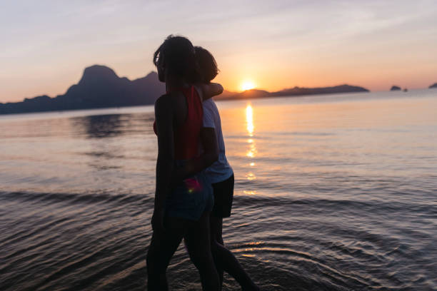 A loving lesbian couple embraces each other while walking on the beach and treading the shallow sea water