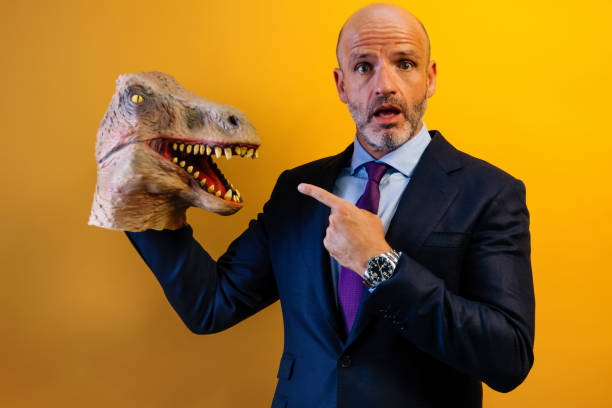 istock A man in a suit is holding a dinosaur puppet. He is pointing at the puppet with his right hand and has a surprised expression on his face 2170498862