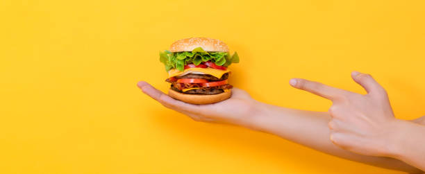 istock Hand pointing to cheeseburger in yellow isolated background banner 2170500809