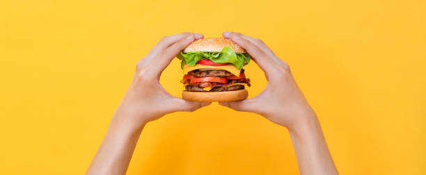 istock Hands holding hamburger on yellow isolated background banner 2170500823