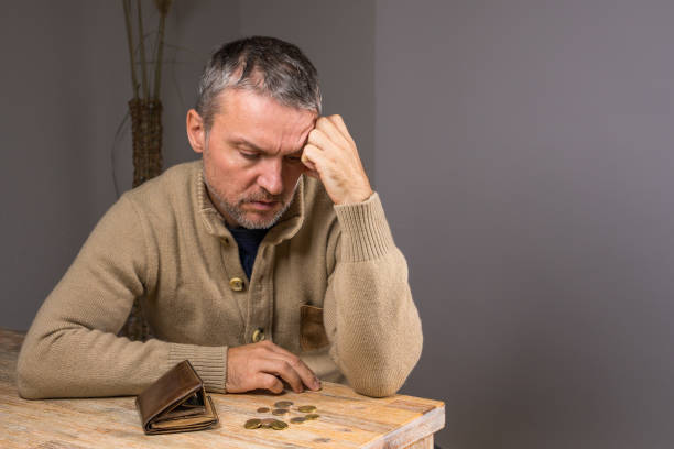istock Middle aged man with beard counts coins. Poor man sits at home, an empty wallet and  last metal coins, money, euros lie in front of him. Financial difficulties 2170511775