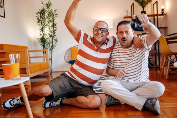 istock Middle age men having fun at home playing video games together while sitting on floor in living room 2170512182