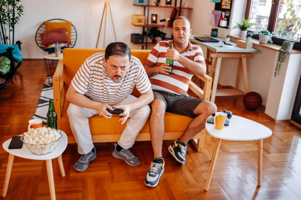 istock Middle age men having fun at home playing video games together while sitting on sofa 2170512352