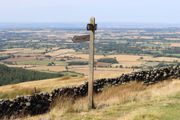 istock Footpath sign on a hillside, with views over countryside fields and woodland 2170528458
