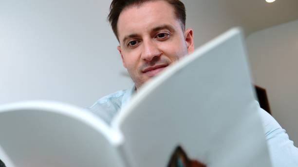 istock Middle age man sit on sofa read fable book increasing imagination. Divergence. 2170528516