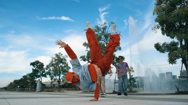 Asian skilled hipster doing freeze pose at camera surrounded by break dancer team near fountain with sky background. Group of handsome people practice b-boy dance. Outdoor sport 2024. Sprightly.