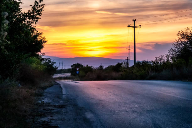 The sun sets over a country road. Mediterranean vegetation, electricity poles