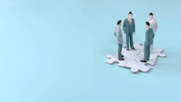 istock Four Miniature Businessmen Standing on Interlocking Jigsaw Puzzle Pieces: Symbolizing Strategic Planning and Collaboration 2170545668