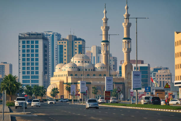Cars drive in downtown Ras Al Khaimah, United Arab Emirates on a sunny day, with the Sheikh Sultan bin Saqr Al Qasimi Mosque in the background