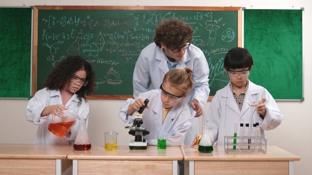 Teenage students and teacher conduct science experiment in junior high school science classroom.  Multi-ethnic group of students ages 13 to 16 years. Male, African descent teacher. Chemistry. Learning, studying.