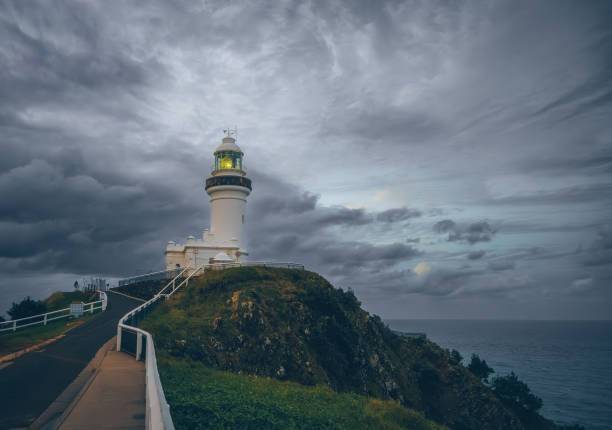 Witness the dramatic beauty of Cape Byron Lighthouse at sunset, perched on cliffs at Byron Bay, Australia, offering stunning views and a picturesque coastal landscape.