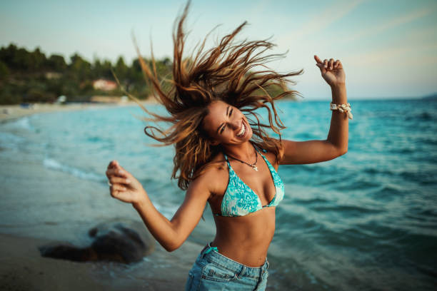 An attractive young woman is having fun and dancing on the beach at the sunset.