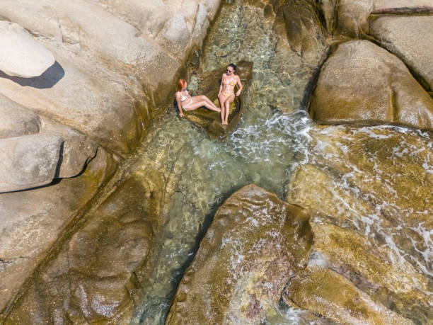 Women enjoy rocky beach of beautiful Aegean sea. Photo is taken on Karydi beach at Sithonia peninsula in Greece.