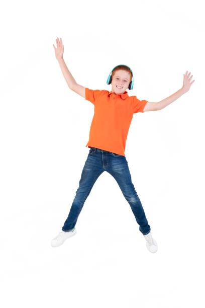 Cute carefree boy dancing, jumping in air, having fun on orange background
