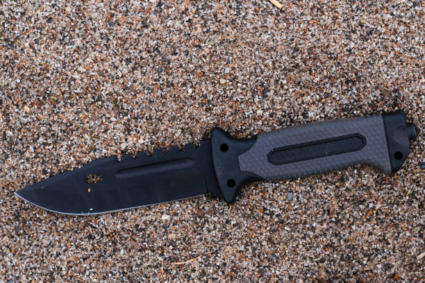 istock Knife with black handle on the sand of a beach. Top view. 2170562874