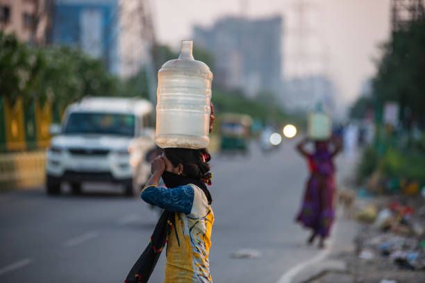Ghaziabad, Uttar Pradesh, India- June 08, 2020: A woman walking down the road with a water container balanced on her head.